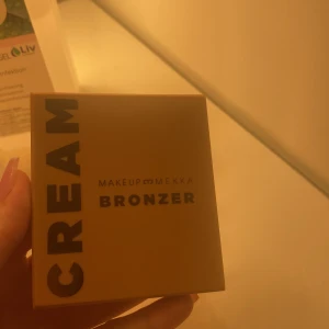 Makeup Mekka Cream Bronzer Warm Breeze - Krämig bronzer från Makeup Mekka i nyansen Warm Breeze. Kommer i en fyrkantig gul förpackning med spegel. Perfekt för att ge ansiktet en solkysst look och enkel att blenda ut tack vare sin mjuka formula.