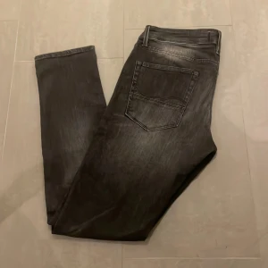 Svarta slim jeans Slim/Glenn - Säljer ett par svarta jeans från Slim/Glenn med snygg tvättad look. Jeansen har klassisk femficksdesign, smal passform och normal midja. Materialet är jeans och färgen är mörksvart med lätt slitningseffekt. Perfekta för dig som gillar en stilren och modern vibe. Jack and Jones!