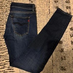 Mörkblå Replay jeans skinny fit - Snygga mörkblå jeans från Replay med klassisk femficksdesign och kontrastsömmar. Modellen har smal passform och tydlig Replay-logga vid fickan. Perfekta för dig som gillar stilrena och moderna jeans med en tight siluett.