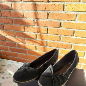Svarta ballerinaskor med rosett, stl 39 - Säljer ett par svarta ballerinaskor från Graceland i storlek 39. Skorna har en snygg rosettdetalj framtill och är gjorda i mocka-liknande material. De har platt sula och rund tå, vilket gör dem både stilrena och bekväma.