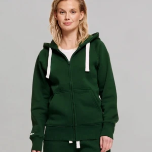 Mörkgrön hoodie från russemerch - Mörkgrön hoodie med vit snörning och dragkedja framtill. Tröjan har huva, ribbade muddar och fickor på magen. Perfekt för chill dagar och enkel att matcha med jeans eller mjukisbyxor. Strlk S men passar typ som M också