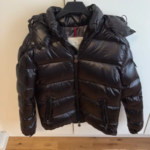 Moncler Maya - En svart Moncler Maya i storlek 1. Prima skick förutom den lilla defekten som syns på sista bilden. Dem 2 knapparna ska gå att knäppa men dem har gett upp tyvärr, går lätt att laga. Knappt använd.