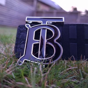 H&M bälte med TB-spänne - Säljer en "H&M" bälte med stort T B spänne i metall. Finns i två varianter: klassiskt rutigt i beige och brunt samt svart med diskret rutmönster. (Man kan byta på sidorna) Bältet är gjort i skinn och har en lyxig känsla, perfekt för att lyfta din outfit. Kontakta för mer information om märket osv🔥