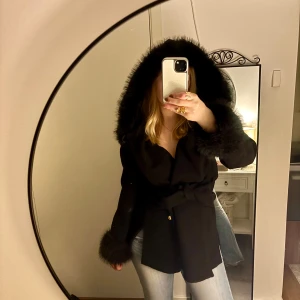 Svart kappa med fuskpäls från Chiara Forthi - Snygg svart kappa från Chiara Forthi med stora fuskpälsdetaljer på huva och ärmslut. Kappan har knytskärp i midjan och guldiga knappar framtill. Perfekt nu till hösten och vintern och håller dig varm 💕 Pälsen är avtagbar på både ärmarna och luvan. En knapp sitter dock lite löst på ena fickan. Använd men annars i gott skick ❤️ storlek xs men passar även xs-m beroende på hur man vill att den ska sitta. Köpt för ca 1300.