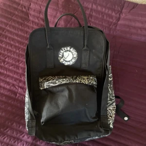  Kånken Art ryggsäck Fjällräven - Cool svart Kånken ryggsäck från Fjällräven med unikt grafiskt mönster på sidor och detaljer. Klassisk fyrkantig form, stort huvudfack, framficka och vadderade axelremmar. Tillverkad i slitstark syntet med logga framtill.