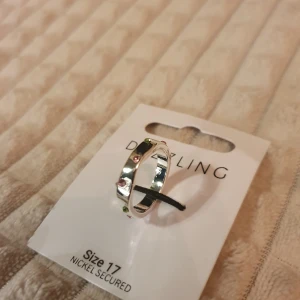 Silverring från dazzling - Säljer ett smycke från Dazzling med en silverfärgad ring i storlek 17 dekorerad med små rosa och gröna stenar.