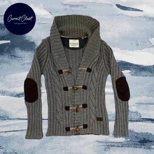 Grå stickad kofta från Lindbergh - Säljer en grå stickad kofta från Lindbergh med grov ribbstickning, stora träknappar och snörning framtill | Bredd: 45cm Längd: 71cm | Size M på pappret men kan passar större.