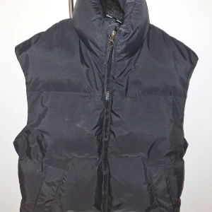 Svart dunväst från H&M - Säljer en svart dunväst från H&M med hög krage och dragkedja framtill. Västen har två snedställda fickor och är tillverkad i ett vattenavvisande material. Perfekt för lager-på-lager och funkar lika bra till jeans som till hoodies.