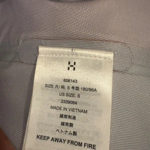 Röd vindjacka från Haglöfs, herr S - Snygg röd och mörkgrå vindjacka från Haglöfs med huva och dragkedja. Jackan har praktiska fickor med dragkedja och stilren logga på bröstet. Perfekt för dig som gillar friluftsliv och vill ha en jacka med cool outdoor-vibe.