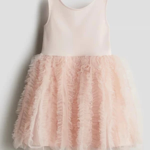 (Flickbarn)Ljusrosa volangklänning med tyll - Supersöt ljusrosa klänning med ärmlös överdel i mjukt tyg och fluffig kjol med flera lager volanger i tyll. Kjolen har en riktigt drömmig känsla och ger extra volym. Perfekt för dig som gillar romantisk och lekfull stil.