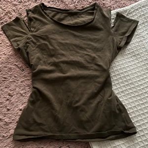 Olivgrön kortärmad topp - Säljer en enkel olivgrön topp med rund hals och korta ärmar. Modellen är figurnära och har en clean look utan detaljer eller mönster. Perfekt för dig som gillar basic och stilrent. Materialet känns mjukt och skönt mot huden.