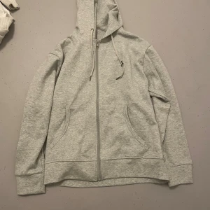 Grå hoodie från Polo Ralph Lauren - Snygg ljusgrå hoodie från Polo Ralph Lauren med dragkedja, huva med snörning och två fickor framtill. Klassisk logga broderad på bröstet. Tillverkad i mjuk bomullsmix, perfekt för chill dagar eller när du vill vara casual.