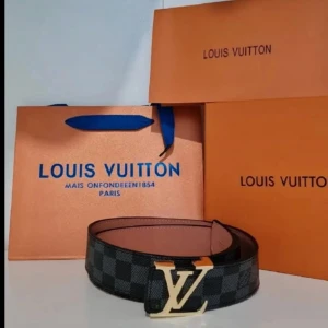 rutigt skärp med guld spänne - Snyggt bälte med klassiskt rutigt mönster i svart och grått. Bältet har ett ikoniskt spänne i guld och är tillverkat i exklusivt skinn. Perfekt accessoar för att lyfta din outfit med en lyxig touch.