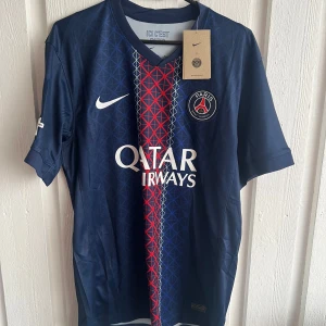 PSG matchtröja Kvaratskhelia #7 Nike - Snygg PSG fotbollströja från Nike med Kvaratskhelia och nummer 7 på ryggen. Tröjan är marinblå med röda och vita detaljer, PSG-emblem på bröstet och Qatar Airways som sponsor. Tillverkad i lätt och ventilerande material, perfekt för fotbollsplanen.