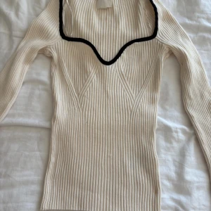Ribbad beige stickad tröja H&M - Ribbstickad beige tröja från H&M med lång ärm och snygg v-ringad halsringning med svart kant. Tröjan har en liten skada som du ser på tredje bilden 