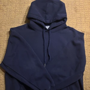 Ami Paris hoodie - Säljer en mörkblå hoodie från Ami Paris med huva och snörning. Tröjan har en snygg patch med Ami-logga på ärmen och är tillverkad i mjuk bomull. Perfekt för dig som gillar stilrena och bekväma plagg med exklusiv känsla.