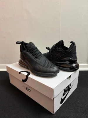 Nike Air Max 270 helsvarta sneakers - Nike Air Max 270 sneakers i helsvart färg med mesh-överdel och synlig Air-enhet i hälen. Snygg, sportig design med snörning och platt sula. Perfekt för dig som gillar stilrena och moderna sneakers med maxad komfort.
