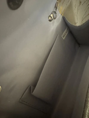 Glittrig silver kuvertväska med kedja - Snygg kuvertväska i glittrigt silver med diagonalrandigt mönster och kedja som axelrem. Perfekt storlek för det viktigaste och har ett fack på insidan. Väskan är stilren och ger en lyxig känsla till din outfit.