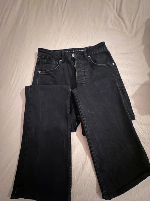 Svarta bootcut jeans, storlek 27/32 - Snygga svarta jeans med boot flare passform och klassisk femficksdesign. Hög midja och långa ben med utsvängda avslut ger en cool siluett. Jeansen är tillverkade i jeansmaterial och har silverfärgade nitar och knapp. Perfekta för dig som gillar en trendig och avslappnad stil.