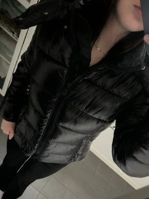 Svart pufferjacka med huva - Säljer en svart pufferjacka med huva och dragkedja framtill från save the duck. Jackan har en glansig finish, quiltade partier och elastiska muddar vid ärmsluten. Den är knappt använd och nypris är 3500kr