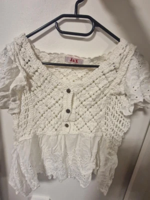 Vit sommrig blus med spets och volang  - Superfin vit blus med virkade detaljer och broderad spets. Blusen har korta puffärmar, volangkant och tre dekorativa knappar framtill. Materialet är bomull med stickade inslag och romantisk känsla. Perfekt för dig som gillar boho-vibe och söta detaljer. Väldigt somrig och oanvänd. Jättebra skicka