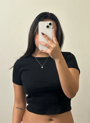 Svart ribbad croppad topp från H&M - Svart croppad topp från H&M med ribbad struktur. Modellen har rund halsringning och korta ärmar. Skriv vid frågor 🥰