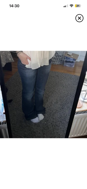 Lågmidjade Blå bootcut jeans - Snygga blå jeans med bootcut passform och låg midja. Jeansen har klassisk femficksdesign och coolt broderi i guld på bakfickorna. Materialet är jeans och färgen är mörkblå med lätt slitning framtill. Perfekt för dig som gillar retrovibe och vill sticka ut.