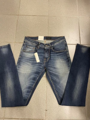 Blå tiger of Sweden  med  W30 L34 - Snygga blå jeans med slitningar och tvättad look, tighta ben och smal fot. Klassisk femficksmodell med orangea sömmar och svart patch bak i midjan. Passar dig som gillar en modern och smal siluett.