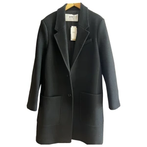 Svart rock från Ami,  Alexandre Mattiussi - Svart rock från Ami Alexandre Mattiussi med klassisk krage, två stora framfickor och knäppning framtill. Stilren och tidlös design i ullmaterial, perfekt för dig som gillar minimalistiska och snygga silhuetter. Passar dig som vill ha en clean look med lite edge. Tror inte jag har lapparna kvar, men kan alltid svara vid frågor eller bilder 😊