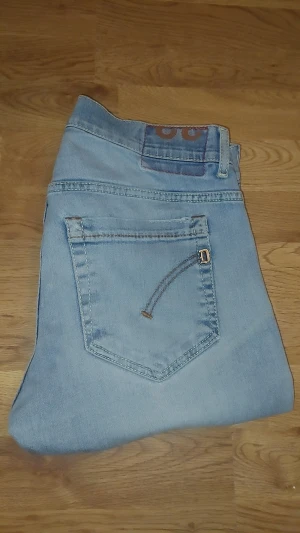 Ljusblå dondup jeans med raka ben - Säljer ett par ljusblå jeans med raka ben och klassisk femficksdesign. Jeansen har knappgylf och snygga detaljer på bakfickorna. Perfekt för dig som gillar en avslappnad och tidlös stil. Materialet är mjukt denim i bomull. Går för ungefär 3500 nypris! Lite mindre i storleken.