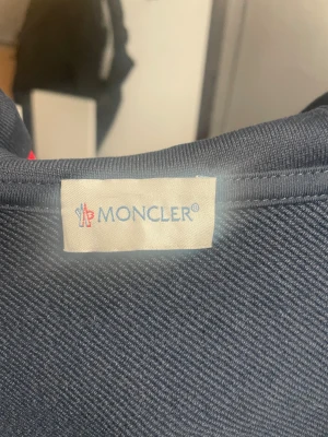 Mörkblå Moncler hoodie med dragkedja - Snygg mörkblå hoodie från Moncler med huva och hel dragkedja. Tröjan har två fickor fram, snörning i huvan och Moncler-logga på ärmen. Ribbade muddar med röd och vit detalj. Perfekt för dig som gillar exklusiva streetwear-vibes obs priset kan sänkas med mycket vid snabb affär.