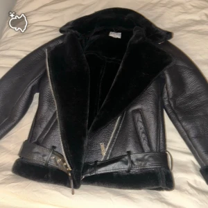 Svart pälsjacka från NA-KD med bälte - Säljer en svart pälsjacka från NA-KD i storlek 34. Jackan har en bred krage, mjuk päls på insidan och detaljer som bälte i midjan och dragkedja framtill. Perfekt för kalla dagar med sin snygga och chunky look. Jag har endast använt den cirka fem gånger och säljer den bara för att den inte riktigt kändes som min stil. Jackan är i jättefint skick.