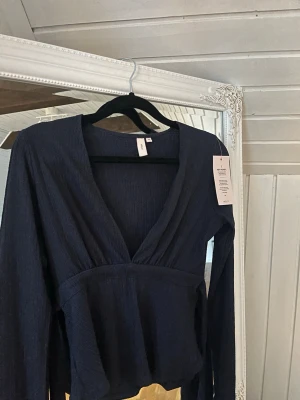 Mörkblå omlottopp från Nelly XS - Snygg mörkblå omlottopp från Nelly i storlek XS. Toppen har ribbad struktur, djup v-ringning och långa ärmar. Perfekt för dig som gillar stilrena och trendiga plagg med lite extra edge. Materialet är mjukt och stretchigt för en bekväm passform. 