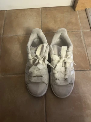 Adidas Campus sneakers i beige mocka - Säljer ett par Adidas Campus sneakers i beige mocka med klassiska vita ränder på sidorna. Skorna har rund tå, platt sula i gummi och breda snören. Perfekt för dig som gillar retrostil och vill ha ett par snygga och bekväma sneakers.