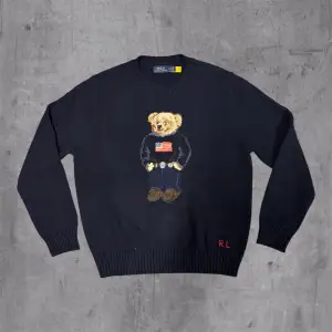 Snygg mörkblå stickad tröja från Polo Ralph Lauren med klassisk Polo Bear broderad på bröstet. Tröjan har rund hals, ribbade muddar och RL-broderi vid nederkanten. Perfekt för dig som gillar ikoniska detaljer och stilren design.