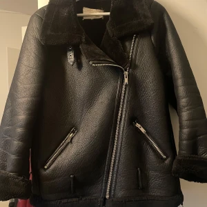 Svart pälsfodrad skinnjacka Zara - Säljer en svart skinnjacka från Zara med pälsfoder och stora slag. Jackan har grova dragkedjor, två snedställda fickor och uppvikta ärmslut med pälsdetaljer. Perfekt för kalla dagar och ger en cool vibe till din outfit.