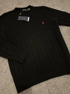 Svart stickad tröja Polo Ralph Lauren - Säljer denna sprillans nya och sjukt snygga svarta kabelstickade tröja från Ralph Lauren. Tröjan är i storlek M, helt nyköpt och med prislappen kvar. Säljs endast pga fel storlek. Priset kan diskuteras.
