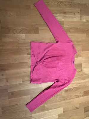Rosa långärmad tröja från Lindex - Säljer en rosa långärmad tröja från Lindex med coolt texturerat tyg och twistad detalj framtill. Tröjan har rund hals och är tillverkad i ett mjukt material som känns skönt mot huden. Perfekt för dig som gillar färg och vill sticka ut lite extra.