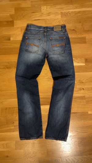 Nudie jeans ”Slim Jim” -  Säljer ett par jeans i storlek W30 L32 från Nudie Jeans med skit fet fade och orange sömmar. Jeansen har raka ben och den klassiska loggan på bakfickan. Jeansen är i topp skick och det finns knappt spår av användning. Färgen är nudies ”Blue Shades”, och modellen Slim Jim.    Måtten är: 38,5cm i midjan, 19cm i fotöppningen och 104cm i ytterbens längd.  Vänligen notera att de kan skilja 0,5cm +/-  Postar inom 24h! Priset är inte hugget i sten och hör av dig såfort du vill veta mera😊