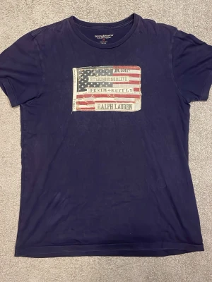 Mörkblå t-shirt Ralph Lauren M - Skitfet mörkblå t-shirt från Ralph Lauren med vintage-tryck på bröstet. Passar till alla olika stilar och går både att klä upp och ner oavsett tillfälle. Tvättas innan den skickas ifall det skulle viljas!                                                                         Skriv vid eventuella frågor🙋                                Pris går att diskuteras vid snabb affär💸