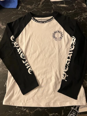 Chrome Hearts longsleeve - Säljer en långärmad svartvit topp från Chrome Hearts med kontrastfärgade ärmar och stort tryck både fram och bak. Tufft logotyptryck längs ärmarna och runt halsen. Materialet är mjuk bomull och modellen har en loose passform med rund hals.