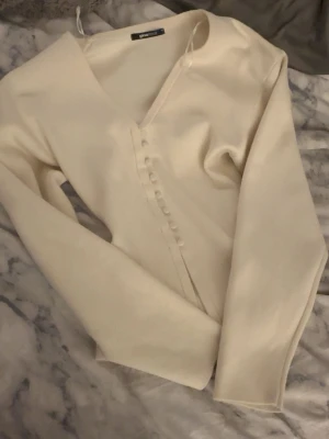 Beige kofta med knappar från Gina Tricot - Supersnygg beige kofta från Gina Tricot med v-ringning och dekorativa knappar framtill. Användt 1 gång