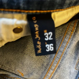 Blå jeans från Nudie Jeans, W32 L36 - Säljer ett par klassiska blå jeans från Nudie Jeans med snyggt slitna detaljer och kontrastsömmar. Modellen har fem fickor och Nudie-loggan på bakfickan. Perfekt passform och riktigt skön denimkänsla.