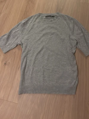 Grå stickad tröja från 157 - Säljer en enkel och stilren grå stickad tröja från 157 med korta ärmar och rund hals. Tröjan har ribbade detaljer vid halsringning, ärmslut och nederkant. Använd fåtal gånger och är i ett bra skick💗