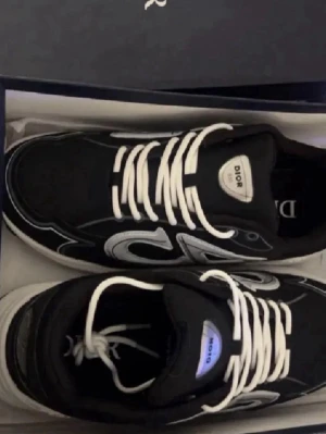 Dior B30 svarta sneakers med vit logga - Säljer ett par Dior B30 sneakers i svart med vit och silverfärgad Dior-logga på sidan. Skorna har rund tå, platt sula och vita snören. Materialet är en mix av mesh och syntet med detaljer 