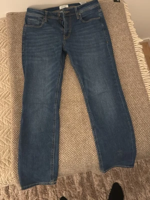  Jack & Jones Jeans - Säljer ett par klassiska blå jeans från Jack & Jones med fem fickor och snygga kontrastsömmar. Jeansen har regular passform och normal midja, tillverkade i slitstarkt bomullsmaterial. Perfekta för en chill och stilren look. Jeansen har endast används max 3 gånger och har inga defekter.