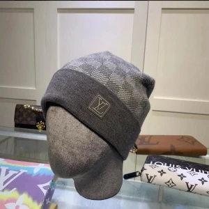 Grå rutig L.V mössa - Snygg grå mössa från L.V med klassiskt rutigt mönster och uppvikt kant. Mössan har en diskret L.V-logga framtill och är stickad i mjukt material som känns lyxigt. Perfekt för dig som vill ha en stilren accessoar med designer-vibe.