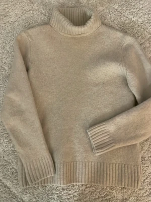 Beige polotröja från Zara - Mysig beige polotröja från Zara i storlek L. Tröjan är stickad med bred ribbad kant vid ärmslut, nederkant och krage. Perfekt för kyliga dagar och enkel att styla till olika outfits känns som S .