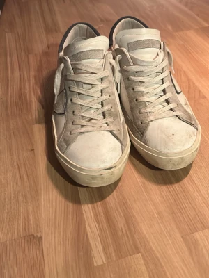 Philipe model skor  - Säljer ett par snygga sneakers i beige och vitt med detaljer i mocka och skinn. Skorna har rund tå, platt sula och snörning framtill. Hälpartiet är mörkare och ger en schysst kontrast. Perfekta för dig som gillar stilrena och neutrala färger.