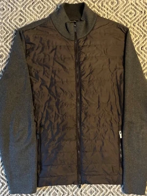Grå cardigan från Massimo Dutti XL - Snygg grå cardiganjacka/bomberjacka från Massimo Dutti i storlek XL. Jackan har quiltad framsida i polyester och stickade ärmar och rygg i bomull och silke. Dragkedja framtill och två fickor med dragkedja. Perfekt för dig som gillar stilren och modern look.